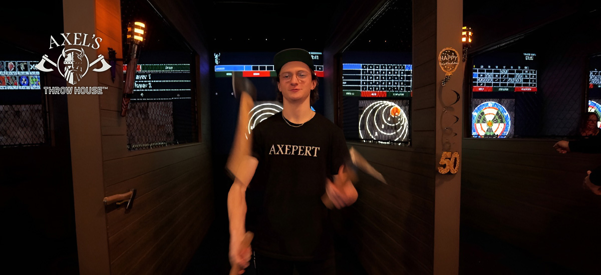An Axel's Throw House employee juggling axes in an axe-throwing lane with a projected game and bullseye in the background